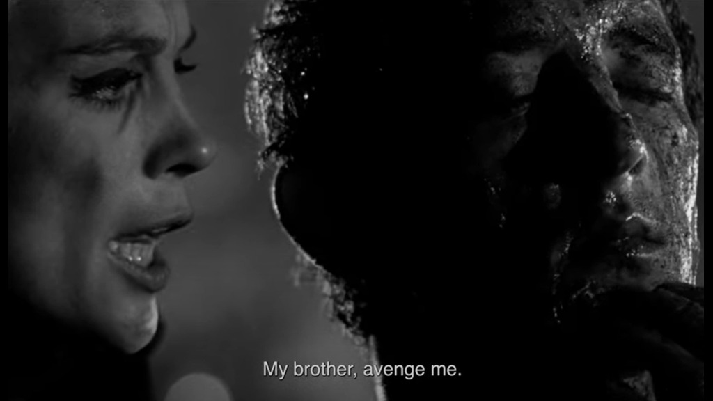 A woman whispers into a dirt-covered male demon. The subtitle reads “My brother, avenge me.”