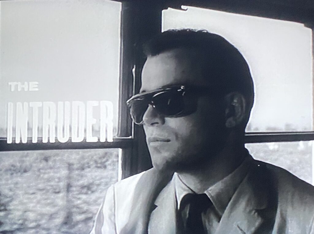 A man in a white suit sits on a bus by the window.