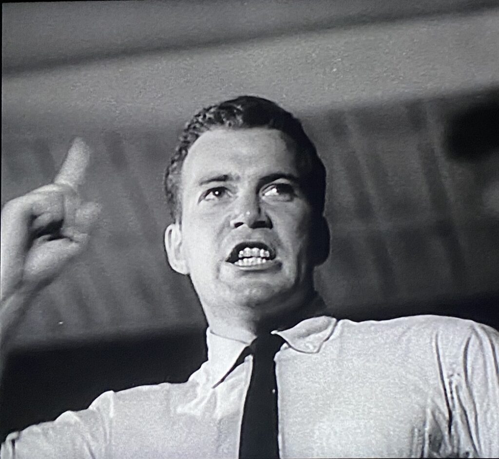 A man in a white suit speaks to a crowd.
