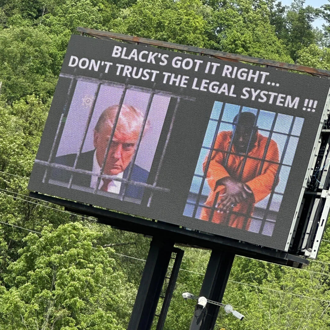 A billboard reading "Black’s got it right… Don’t trust the legal system!!!” with a picture of Trump’s mugshot on the right  and a Black man wearing an orange jumpsuit, behind bars, on the left.