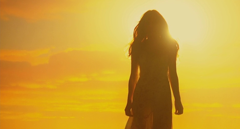 A woman stands in front of a sunrise.