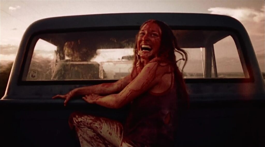 Sally in the back of a speeding truck, covered in blood and horror and trauma, cackling wildly with survival, looking back at the nightmare she escaped.