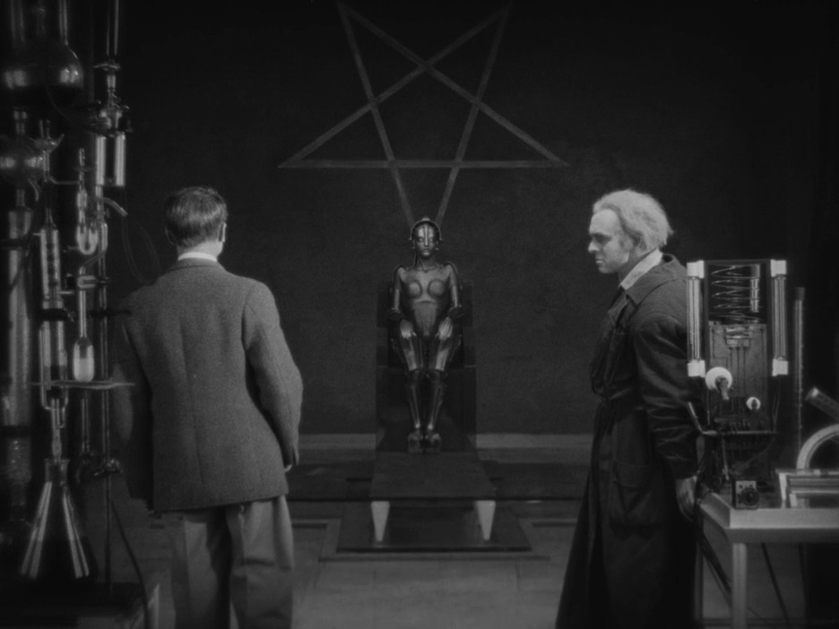 Two men stand to the side of a seated robot.