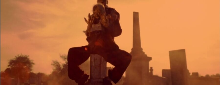 An utterly gruesome pair of fetid dead bodies lashed together and perched on a tombstone, in the arid Texas sky