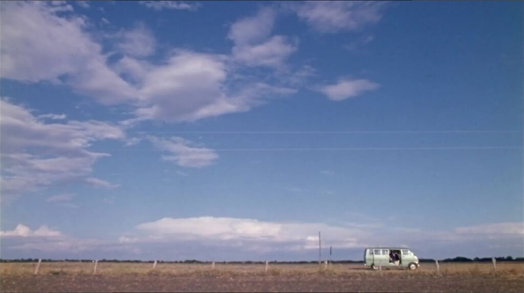 Still frame of a beautiful shot of the natural grandeur of America, with the hitchhiker entering the van, in the foreground.