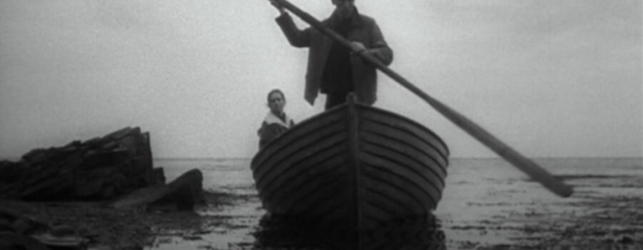 Max Von Sydow (Johan) and Liv Ullman (Alma) arrive at their island getaway. Johan Stands in a large row boat, reflected in dark water, rocky shore nearby.