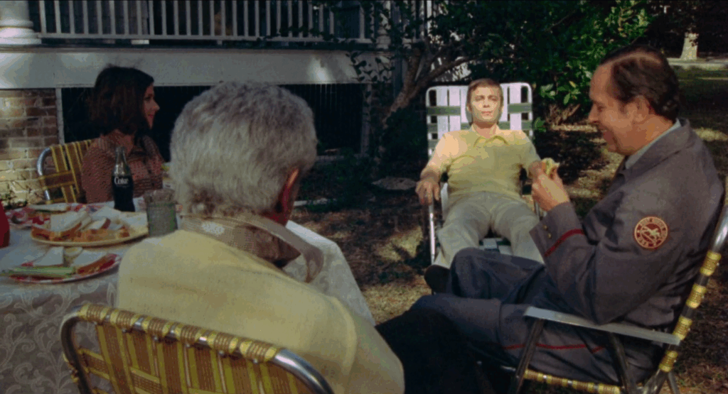 a pale young man in a white chair picnics with a group of people in
yellow chairs.