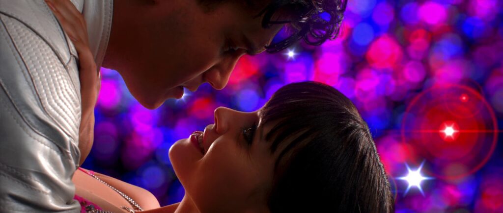 A young man and young woman lean in for a kiss in front of a dazzling red and blue background