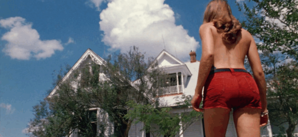 Under a bright summer sky, a young woman approaches an intimidating, two-story house with white siding