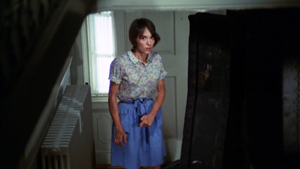a brunette woman standing on a staircase looking scared