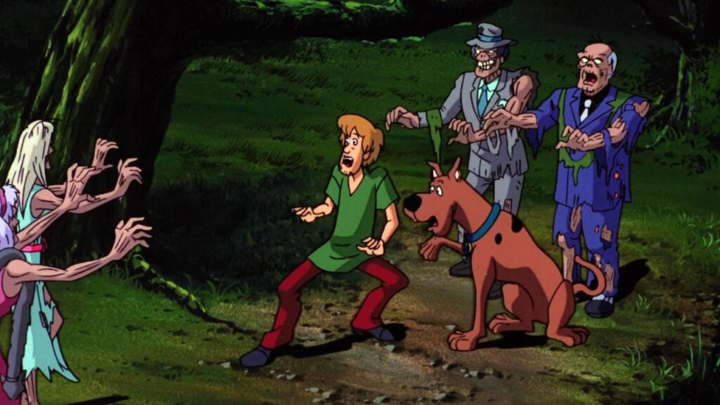Brown dog looks frightened next to a frightened blonde man in a green shirt. Five zombies walk towards them from either side.