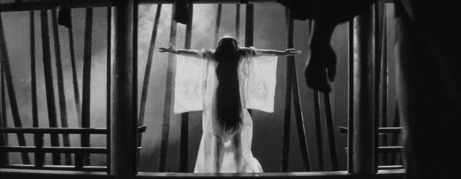 Center, a woman stands, arms outstretched to her sides, in a translucent kimono. Right, a man’s hand lurks in silhouette.