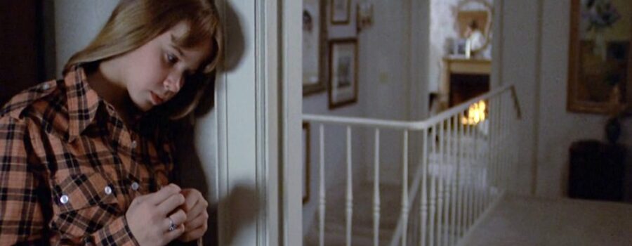 A concerned Regan bows her head and leans against the wall near the door of her bedroom to listen to her mother in the other room.