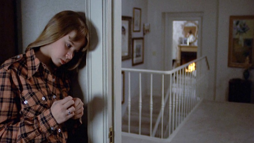 A concerned Regan bows her head and leans against the wall near the door of her bedroom to listen to her mother in the other room.