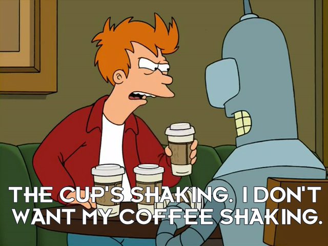 Redhaired man in a red jacket and white shirt holds a cup of coffee with two empty coffee cups in front of him. He sits at a table in front of a grey robot.