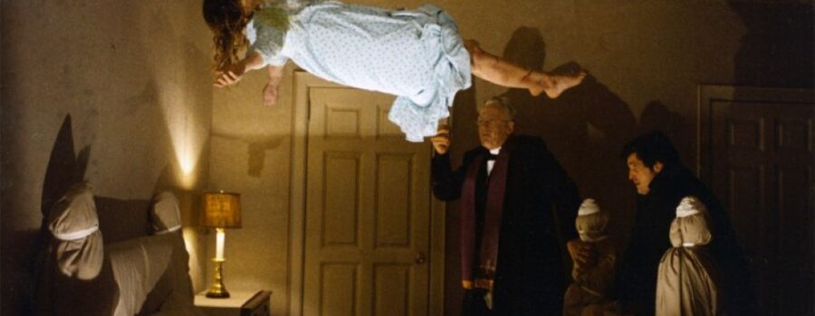 Linda Blair as Regan hovers over her bed in a light blue nightgown as Father Karras and Father Merrin pray next to the bed.