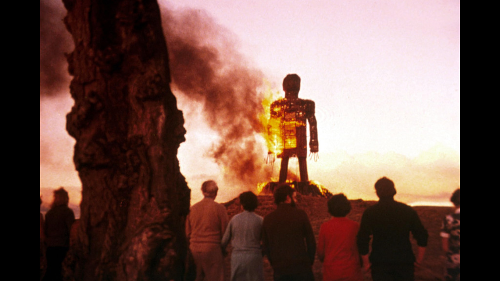 A massive wooden man-shaped structure burns at sunset.
