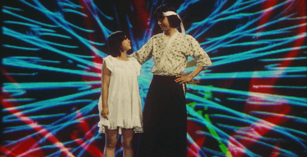 A cowboy-style two-shot of Yuka on the left and Koji (played by Ryôichi Takayanagi) on the right, looking at each other with admiration and jubilation. They are superimposed against a kaleidoscopic cyan and red splatter, Yuka dressed in a white short-sleeved nightgown and Koji in his kendo uniform. Koji's right hand is extended and relaxed on Yuka's right shoulder, with his left hand resting on his left hip. His smile is closed-lipped but defined while hers is open-jawed--perhaps even laughing.