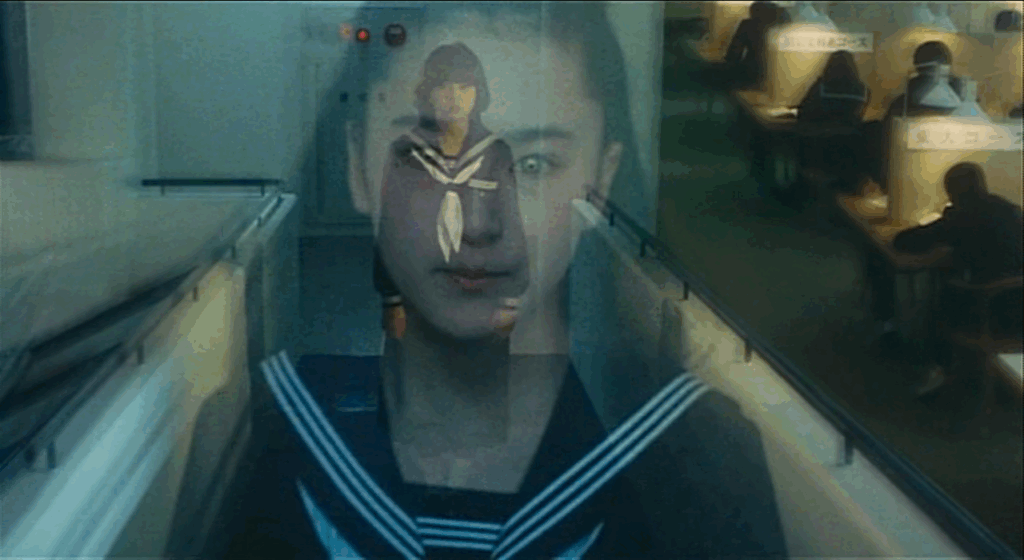 A double-exposed long shot of Yuka, dead center of frame, standing in her school uniform in a nondescript walkway with railings on either side of her, combined with a medium close-up of Michiru (played by Masami Hasegawa) in the same uniform, her piercing green eyes and emotionless expression overlaying Yuka's look of trepidation and horror. While the majority of the shot has a blue tint to it, in the background of the right-hand side of the frame are students hunkered over orange-lit study spaces in soft focus.