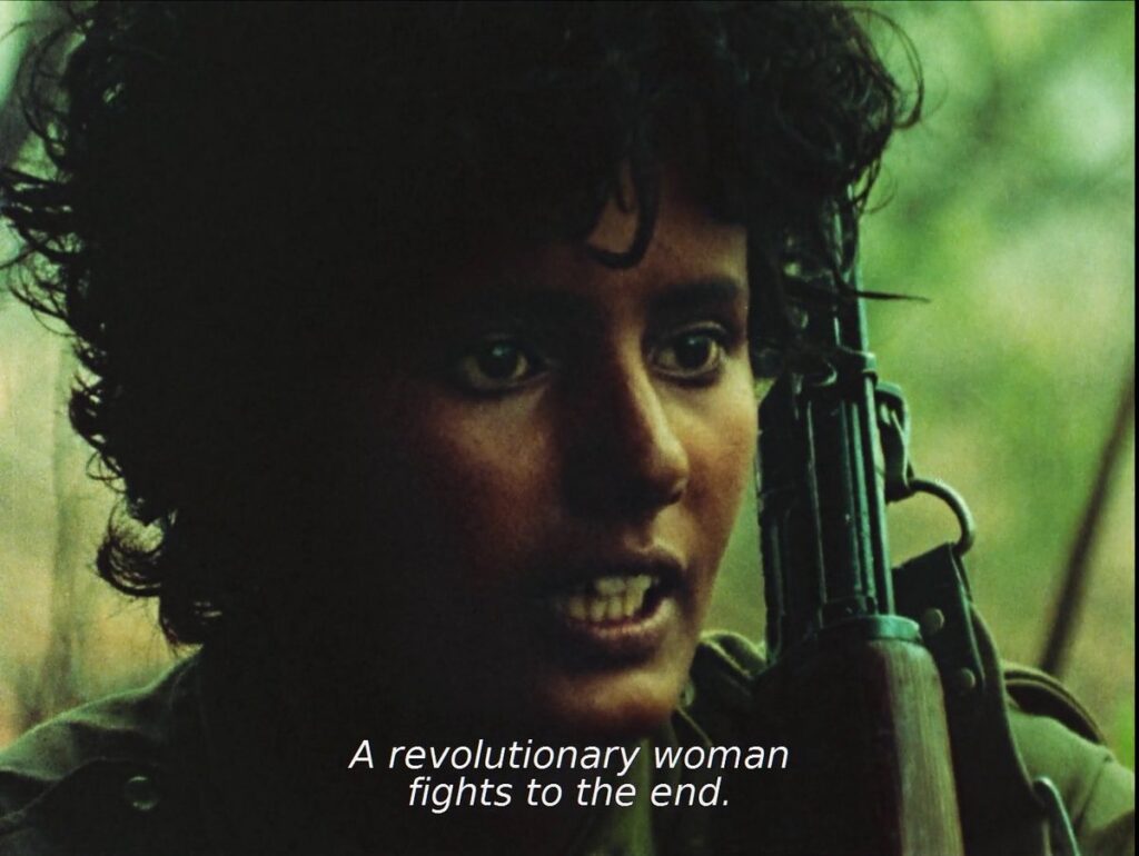 Closeup of young woman with short dark hair facing camera and explaining, as the caption says, ‘A revolutionary woman fights to the end’.