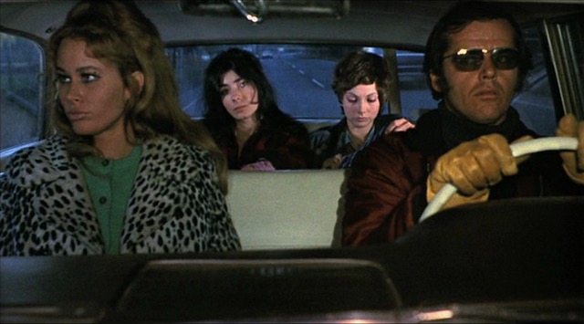 A man wearing sunglasses and driving gloves drives three women in a car.