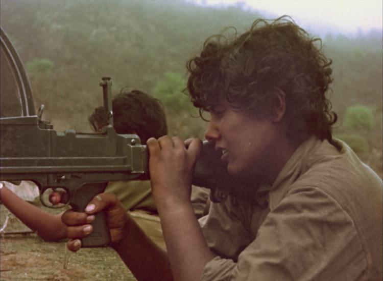 Two women in military uniform shooting guns over top of a rock.