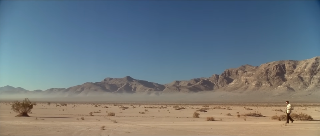 An extreme wide shot of the Nevada desert featuring a man, Robert De Niro, in a white jacket and black pants.