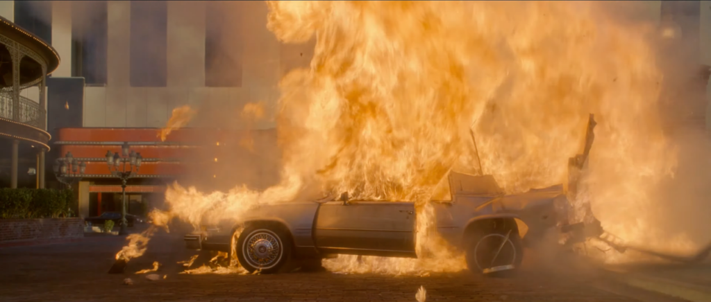  A wide shot of an exploding 1982 Cadillac Eldorado engulfed in flame in a parking lot