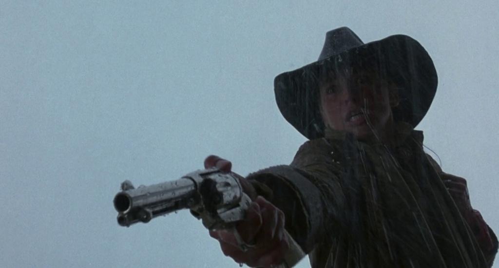 Ellen “The Lady” McKenzie (Sharon Stone) stands in the rain with her jacket and cowboy hat, fury in her face, pointing her gun toward the ground at a figure offscreen.