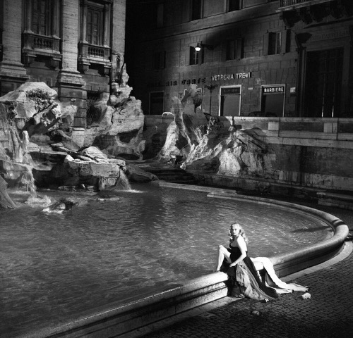black-and-white image of a white, blonde woman sitting on the edge of a fountain