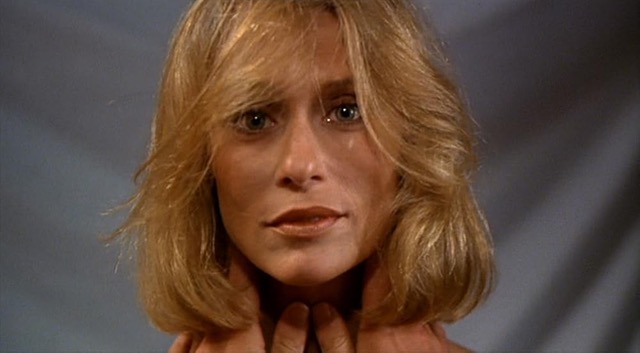 Lauren Hutton looking into the camera, smiling slightly with some of her hair falling in front of her face and hands caressing her neck.