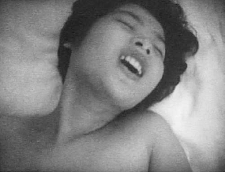 a close up shot of a woman, naked, with her head on her pillow. she is leaning back with her eyes closed and mouth open. the image is in black and white