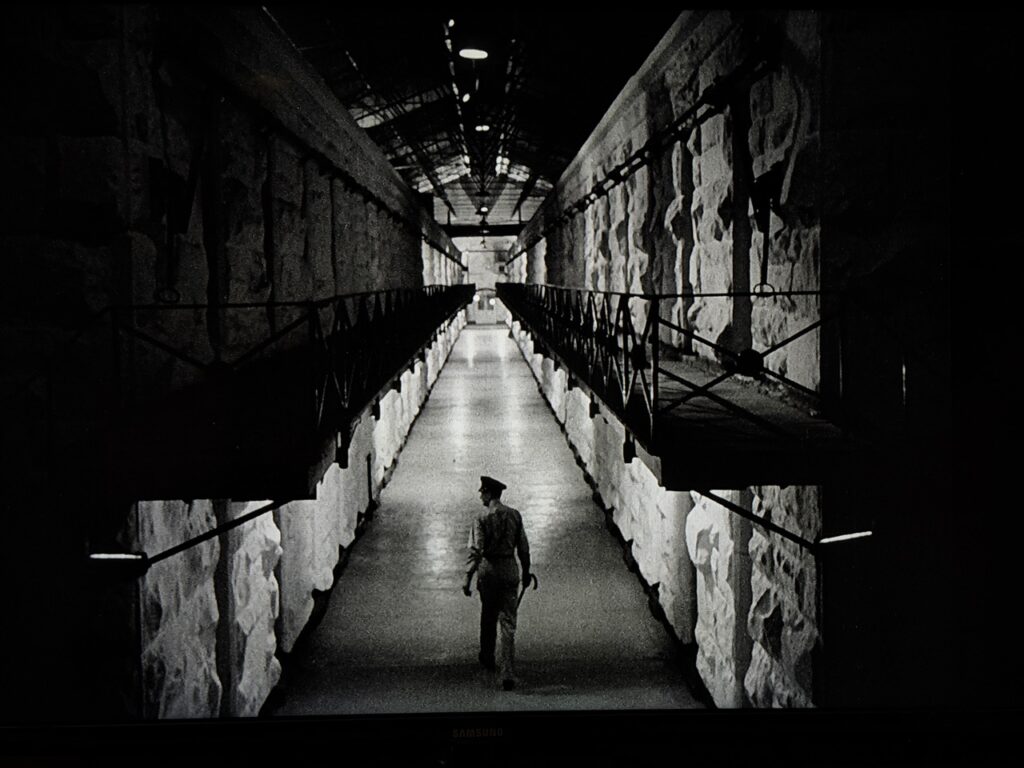 Wide-angle shot of a prison cell block with two tiers of cells.
