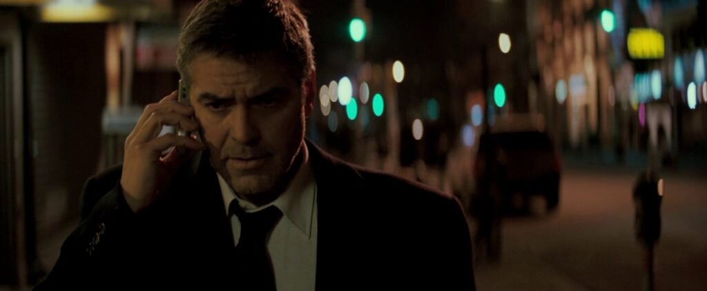 Michael Clayton (George Clooney) walks down a dark New York street at night, talking on his mid-2000’s flip phone with a stern look on his face.