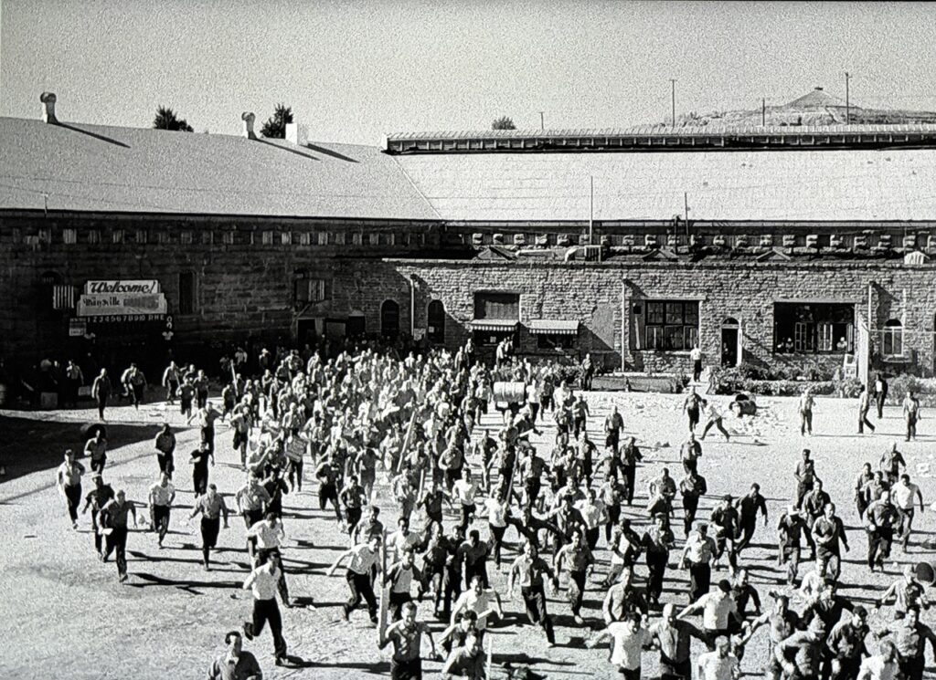Wide-angle image of prisoners running riot across a prison exercise yard.