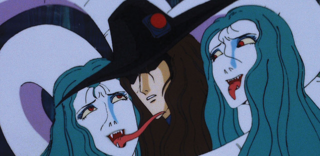 The faces of two snake women with green hair flank the face of a man in a wide brimmed hat and brown hair. The woman on the left licks the man’s face with her long tongue.