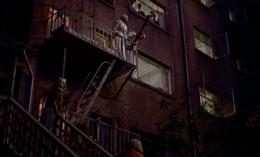 a man and woman standing on the fire escape of an apartment complex