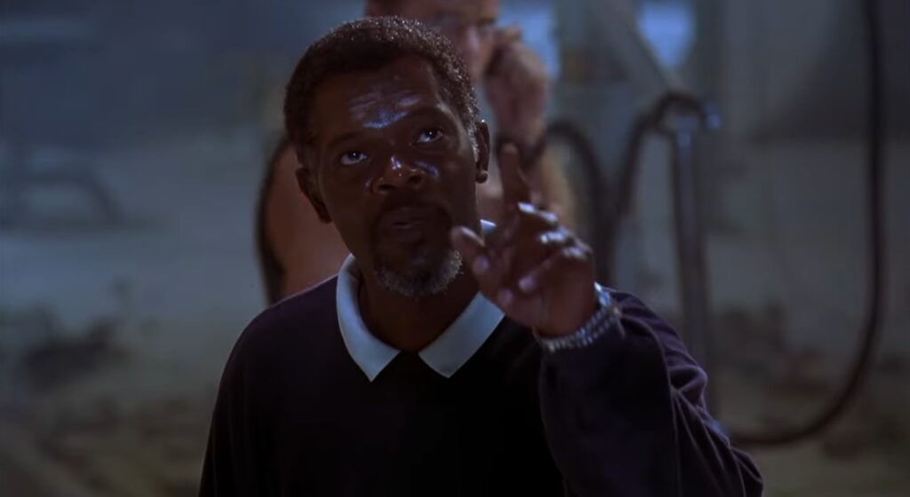 Samuel L. Jackson, wearing a sweater, points in disbelief at a genetically enhanced shark