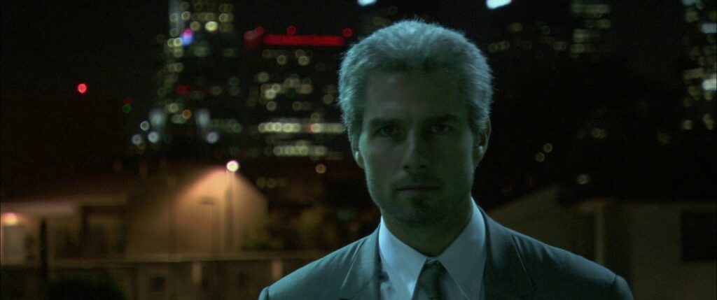 Vincent (Tom Cruise), a grey-haired hitman in a nice grey suit, stares intensely forward, in front of the blurry outline of downtown Los Angeles.