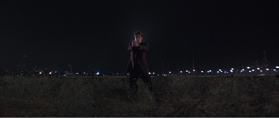 A man standing in an airport field with a gun drawn.