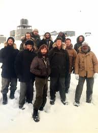 Kurt Russell, Keith David, and the cast of John Carpenter’s The Thing stand outside in arctic tundra for a promotional still for the film.