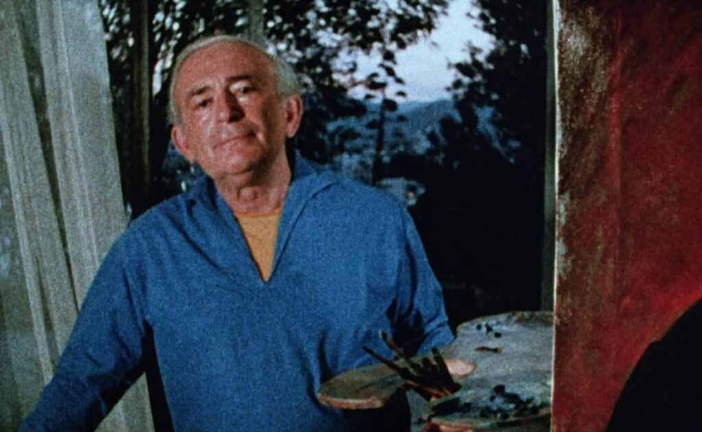 An elderly man holding a painter’s palette.