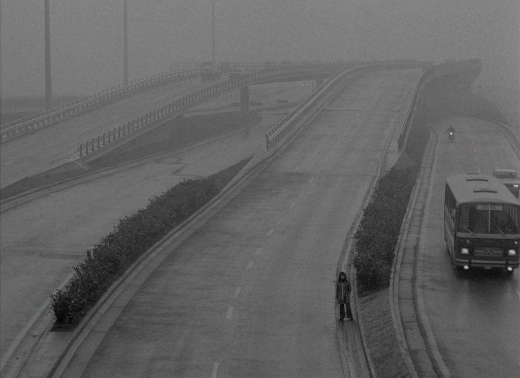  Julie (Chantal Akerman) standing on the side of an empty, foggy highway