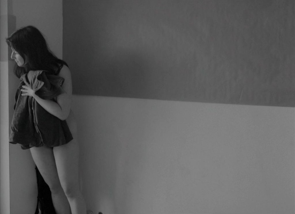  Julie (Chantal Akerman) naked, wrapped up in a blanket, standing in the corner of her room looking out the window.