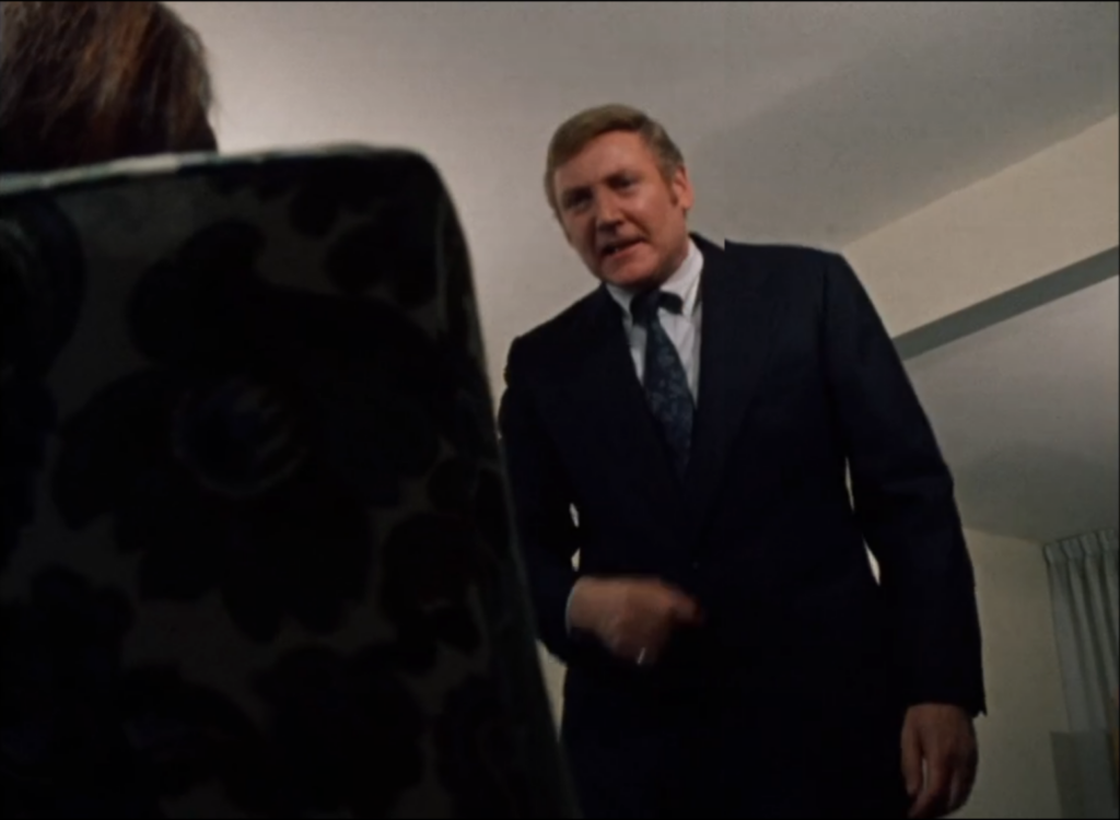 A man aggressively looms over a woman sitting in a chair.