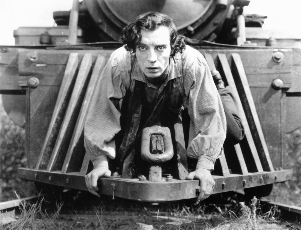 Black and white image - a man holds tightly to a moving train with a determined look on his face.