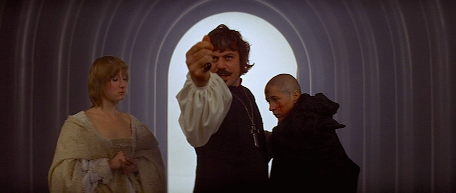 Madeleine (Gemma Jones) looking at Father Urbain Grandier (Oliver Reed) holding up his hand towards nearby witnesses next to one of the nuns after she had been committing sin.