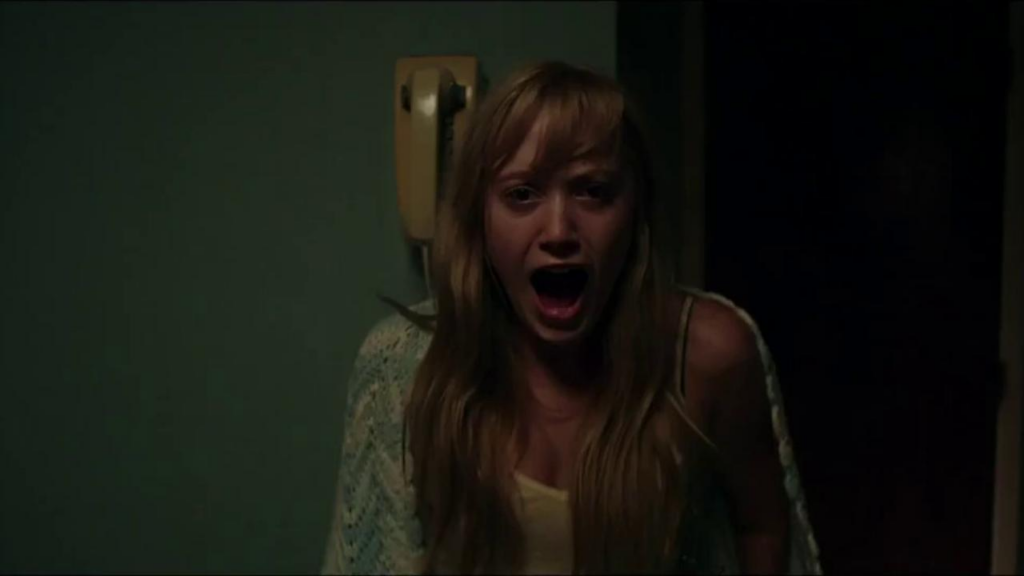 Jay, the teenage final girl from It Follows, stands in her kitchen, momentarily unable to move from fear, screaming at whatever terror she sees just behind the camera.